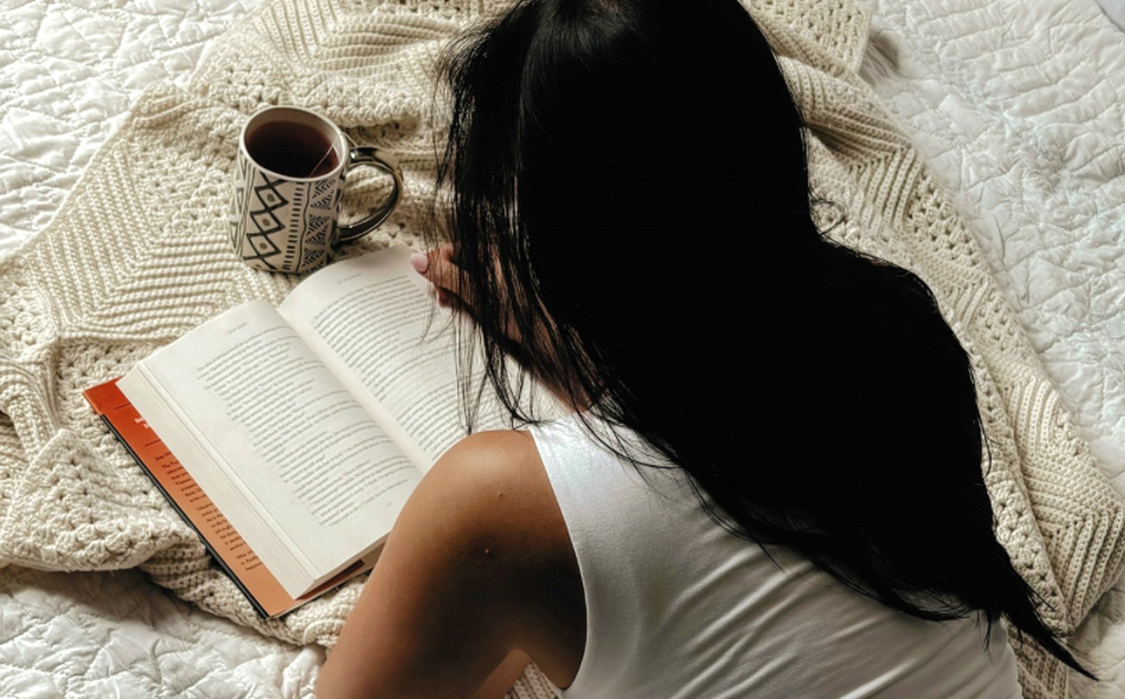 A woman relaxing on a cozy blanket with a book and a cup of tea